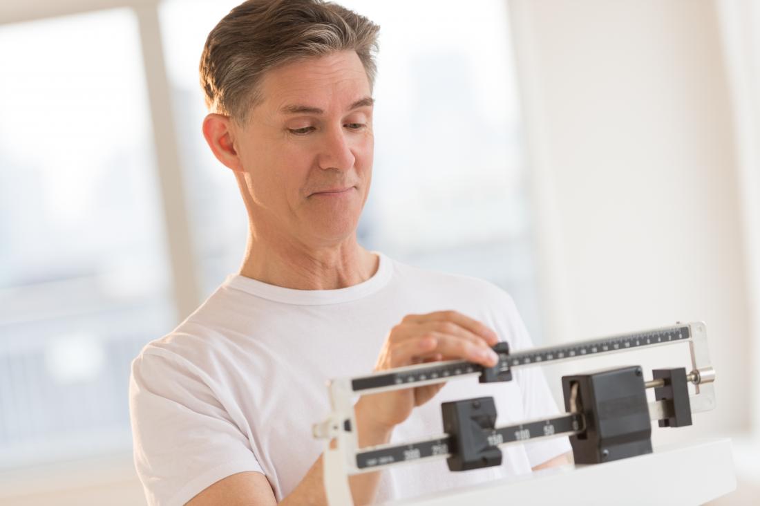 Underweight man standing on weighing scales trying to gain weight safely.